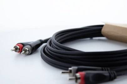 Długi kabel audio z dwoma wtyczkami RCA, czerwoną i białą, leży zwinięty na białoszarym tle.