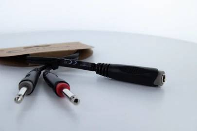 Dwa wtyki audio jack 6,35 mm, jeden czarny, drugi oznaczony na czerwono, oraz adapter, leżące na białym tle.