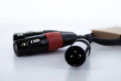 Kilka kabli audio z wtyczkami XLR leży na białym podłożu. Jeden z kabli posiada czerwony pierścień.