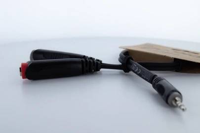 Kabel adapter z wtyczką jack 3,5 mm i dwoma gniazdami RCA, czarne, leżące na białym tle.