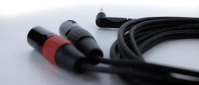 Dwa kable XLR z czerwono-czarnymi złączami rozmazują się na pierwszym planie, połączone pod kątem wtyczką jack 3,5 mm.