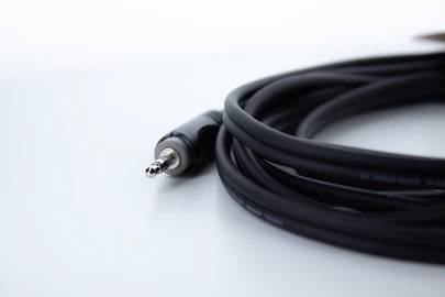 Czarny kabel audio z srebrnym wtykiem jack 3,5 mm leży na białym tle.