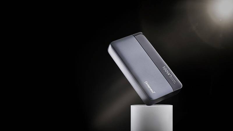 Czarny, przenośny powerbank lekko pochylony unosi się nad cylindrycznym cokołem na czarnym tle.