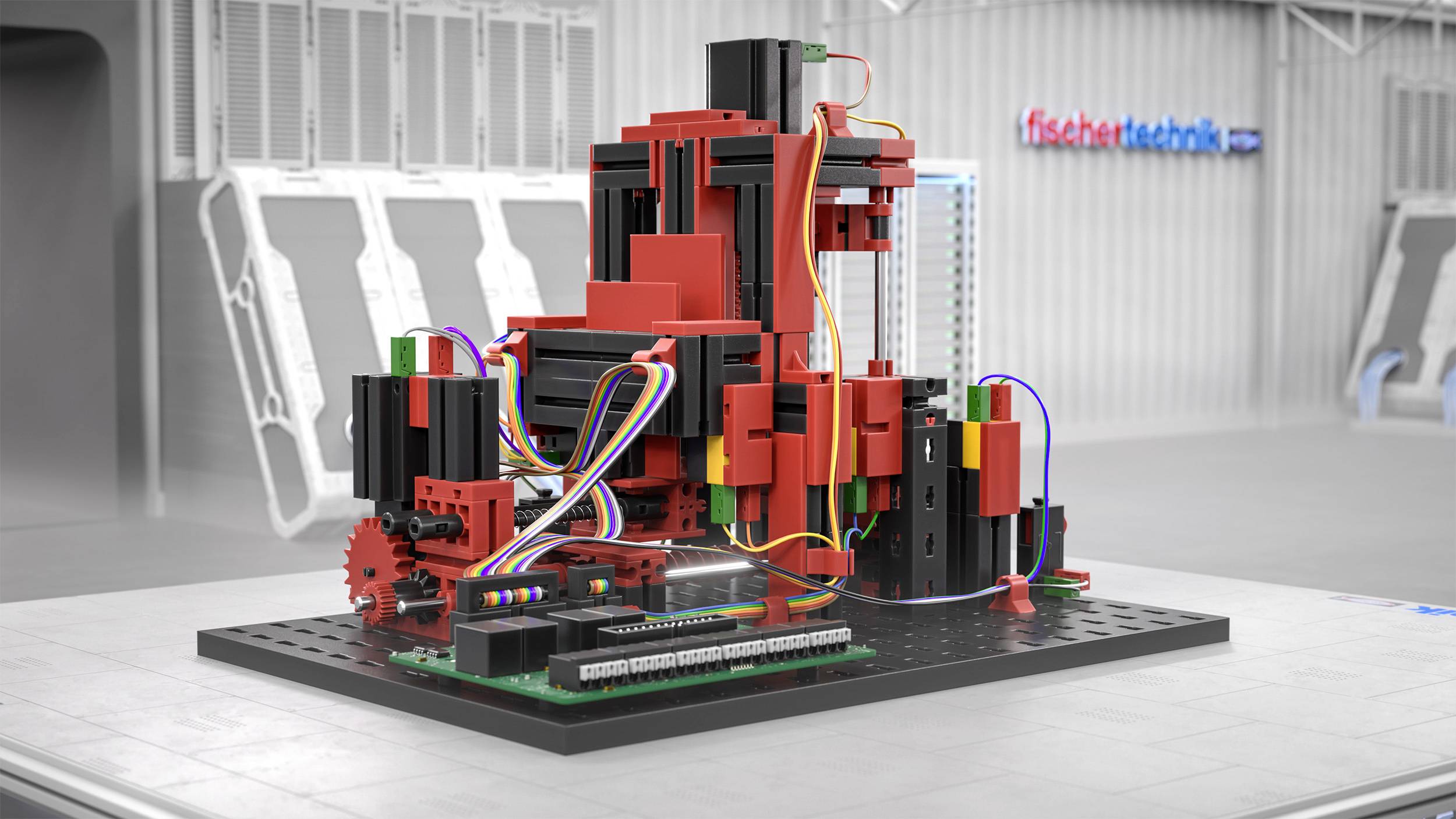 Model złożony z czerwonych i czarnych elementów konstrukcyjnych z kolorowymi kablami na podstawie, otoczony sprzętem technicznym w pomieszczeniu.