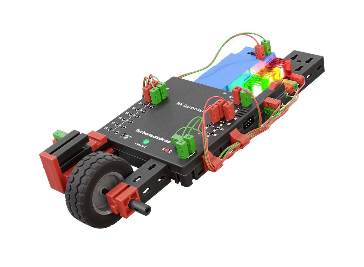 Mały robot z zestawu montażowego z wieloma połączonymi przewodami komponentami i diodami LED, umieszczony na czarnej platformie z kółkami.