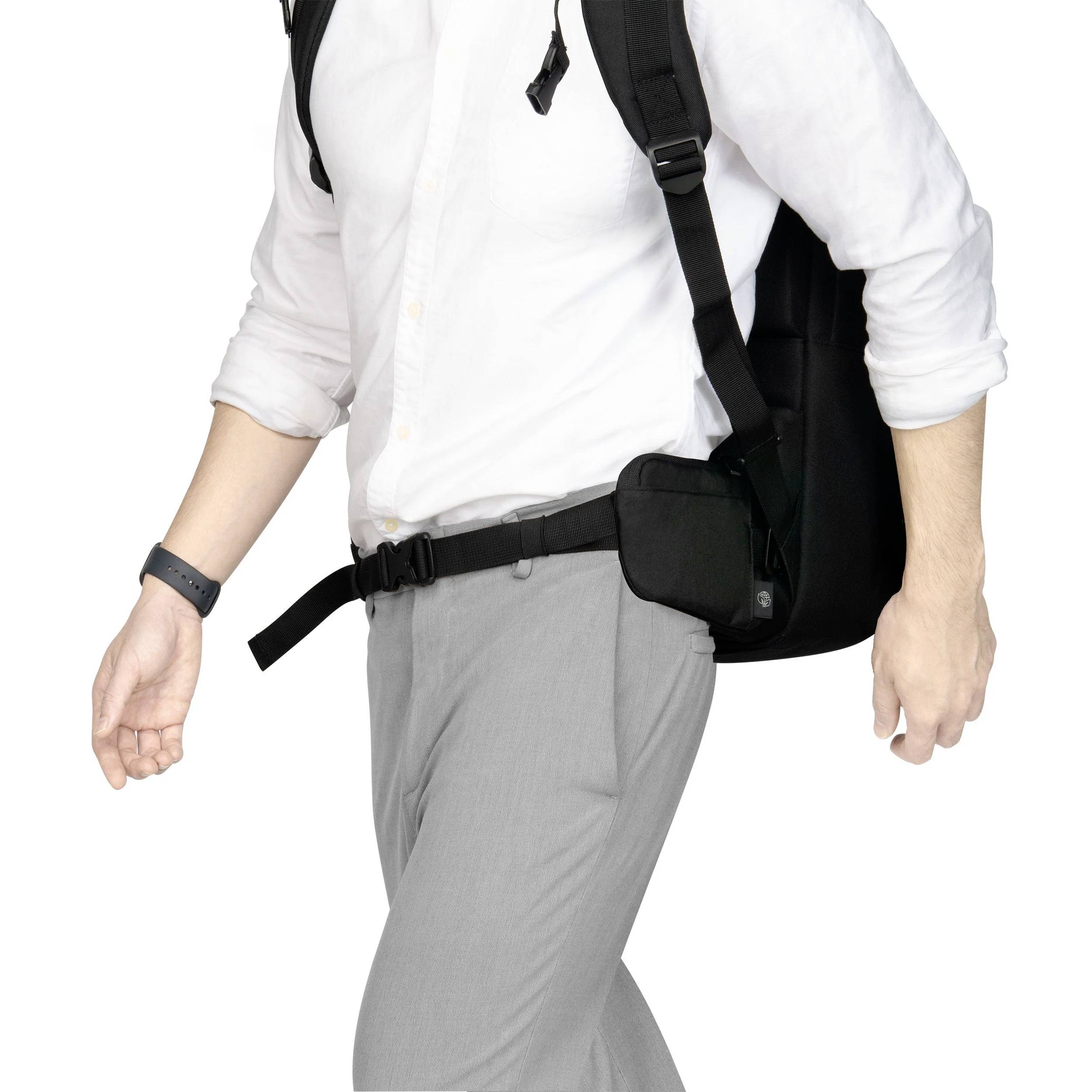 Mężczyzna w białej koszuli i szarych spodniach nosi plecak i czarną saszetkę, idzie szybkim krokiem z opuszczoną głową.