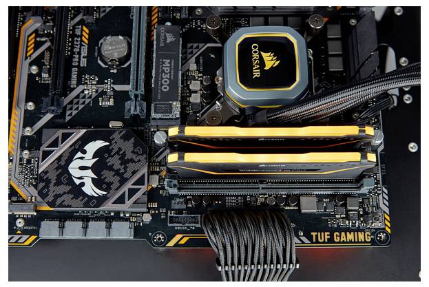 Zbliżenie płyty głównej komputera z modułami RAM i radatorami, z widocznymi logo 'TUF Gaming' i 'Corsair'.