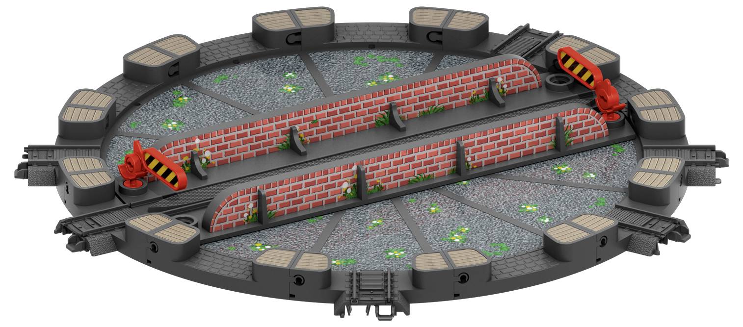 Okrągły model obrotowej platformy z trzema czerwonymi zaporami i torami. Platforma obrotowa spoczywa na szarym podłożu porośniętym roślinami.