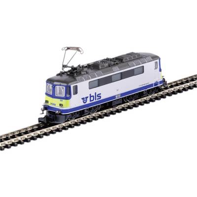 Niebieskobiały pociąg modelowy z napisem 'BLS' jedzie po torach. Pociąg posiada pantograficzny odbierak prądu.