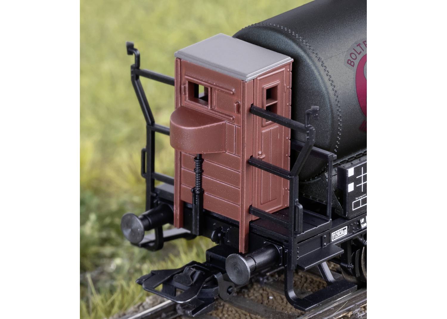 Model sprzęgu kolejowego z czerwonobrązowym domkiem hamulcowego, otaczającym terenem i torami w szczegółowym ujęciu.