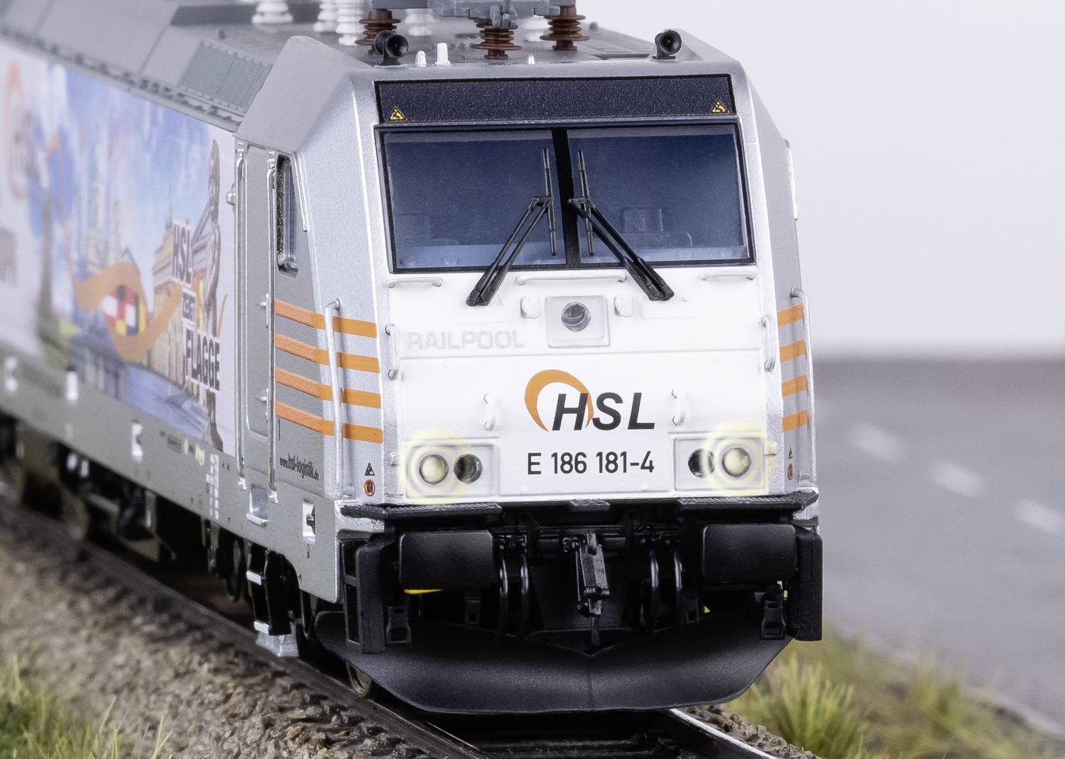 Lokomotywa kolejki modelarskiej na torach z reklamą na boku, prezentująca szczegółowe struktury wagonu i torowiska.