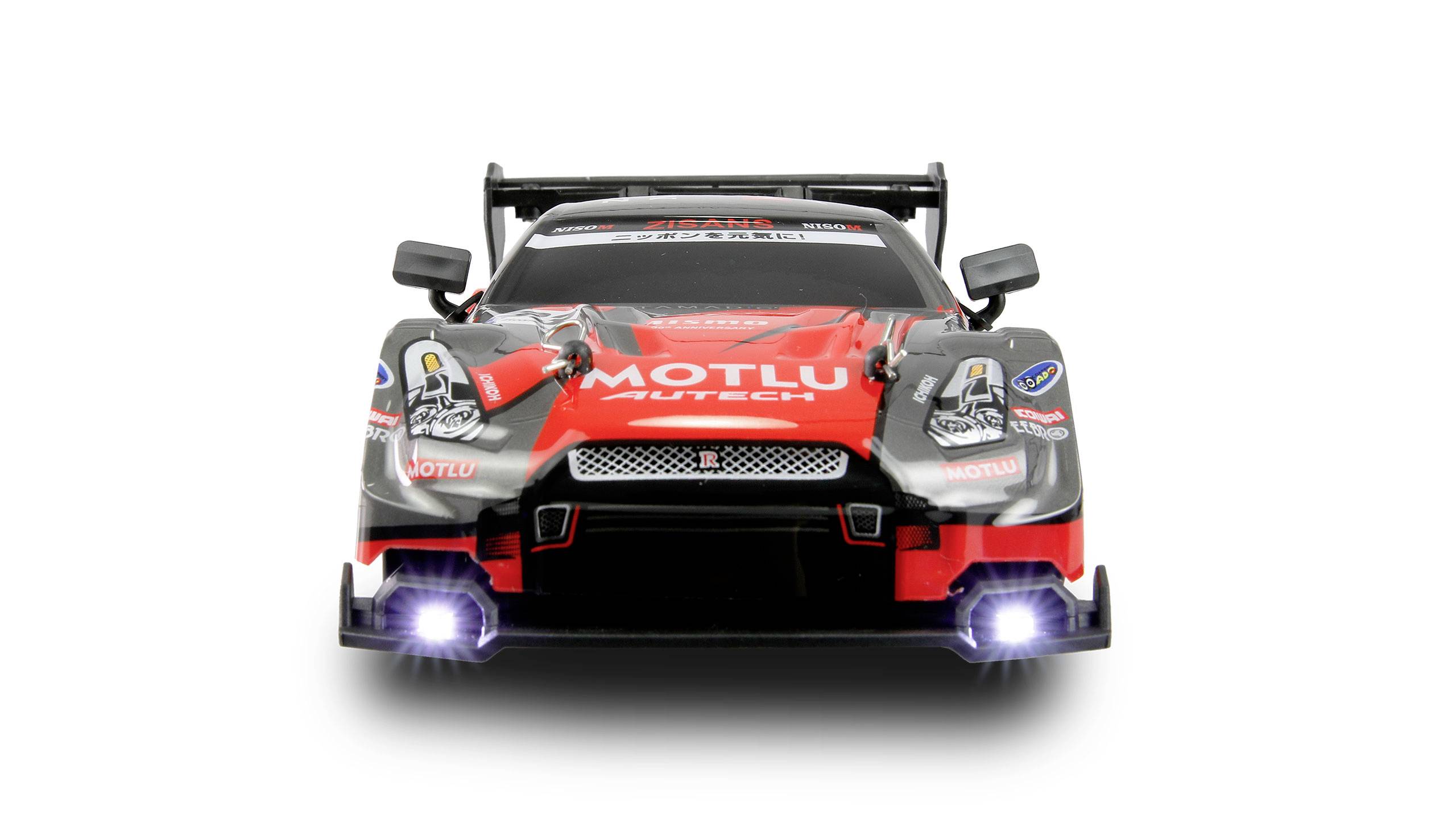 Czerwony samochód modelowy z naklejkami z serii wyścigowej jedzie prosto na widza. Światła przednie są włączone.