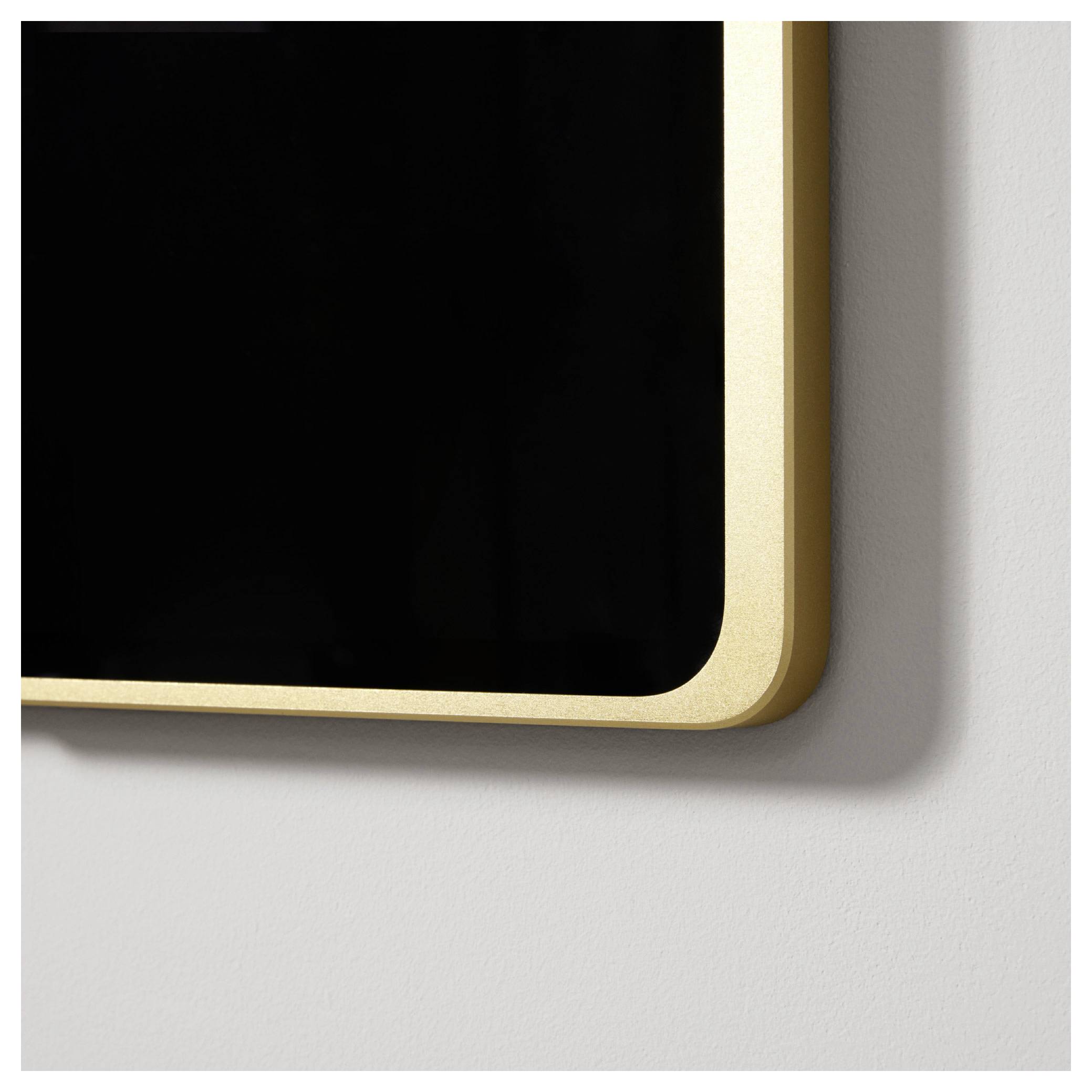 Prostokątne lustro ścienne w złotej ramie, zawieszone na białej ścianie.