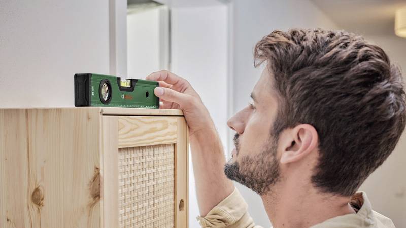 Mężczyzna mierzy wysokość szafy poziomicą w jasnym pomieszczeniu.