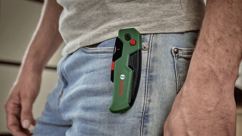 Mężczyzna nosi złożony zielony scyzoryk firmy Bosch w prawej kieszeni dżinsów. Nóż posiada czerwony przycisk.