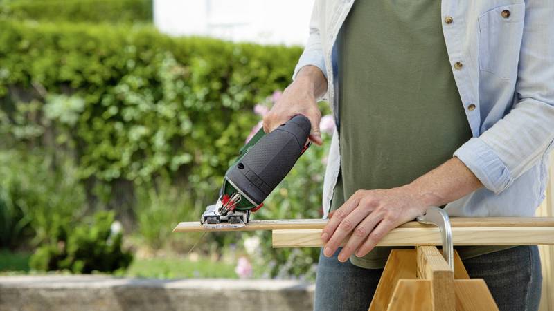 Osoba przecina elektryczną piłą deskę drewnianą na wolnym powietrzu.