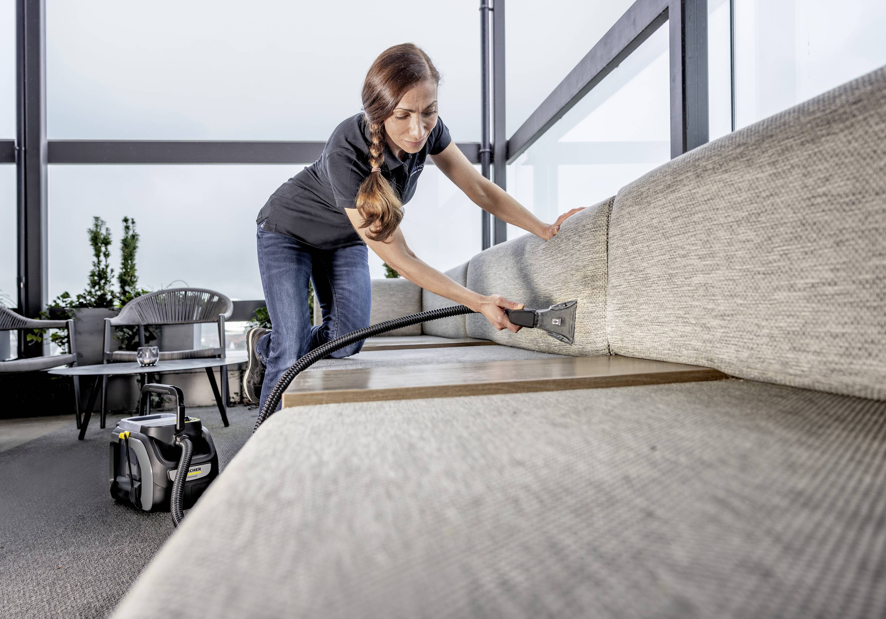 Osoba odkurza duży kanapa odkurzaczem w nowoczesnym, dobrze oświetlonym pomieszczeniu.