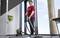 Osoba w czerwonej koszulce odkurza dywanową podłogę w nowoczesnym pomieszczeniu biurowym, z widocznym oknem i rośliną w tle.