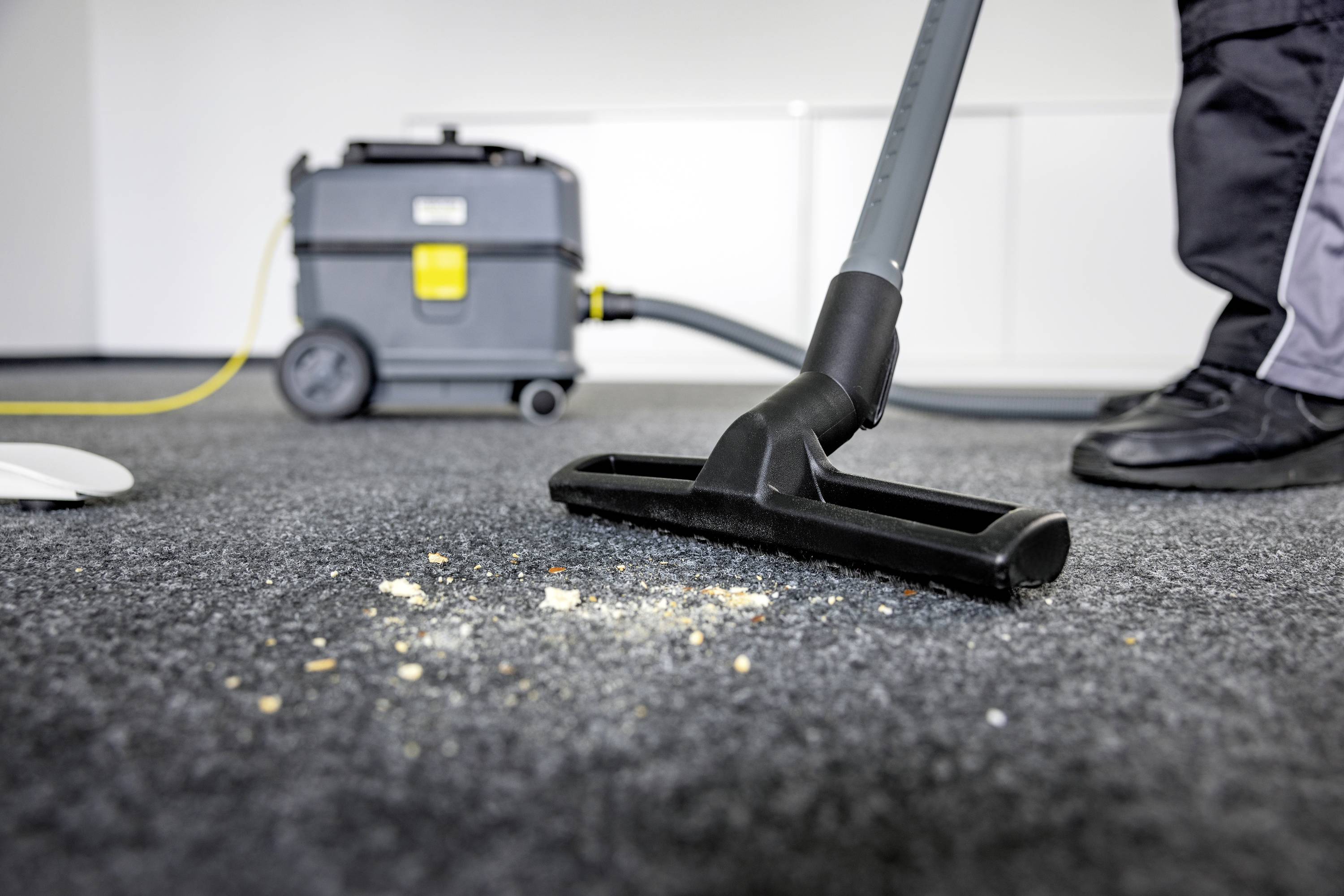 Osoba odkurza dywan odkurzaczem. W tle widać sprzęt czyszczący.