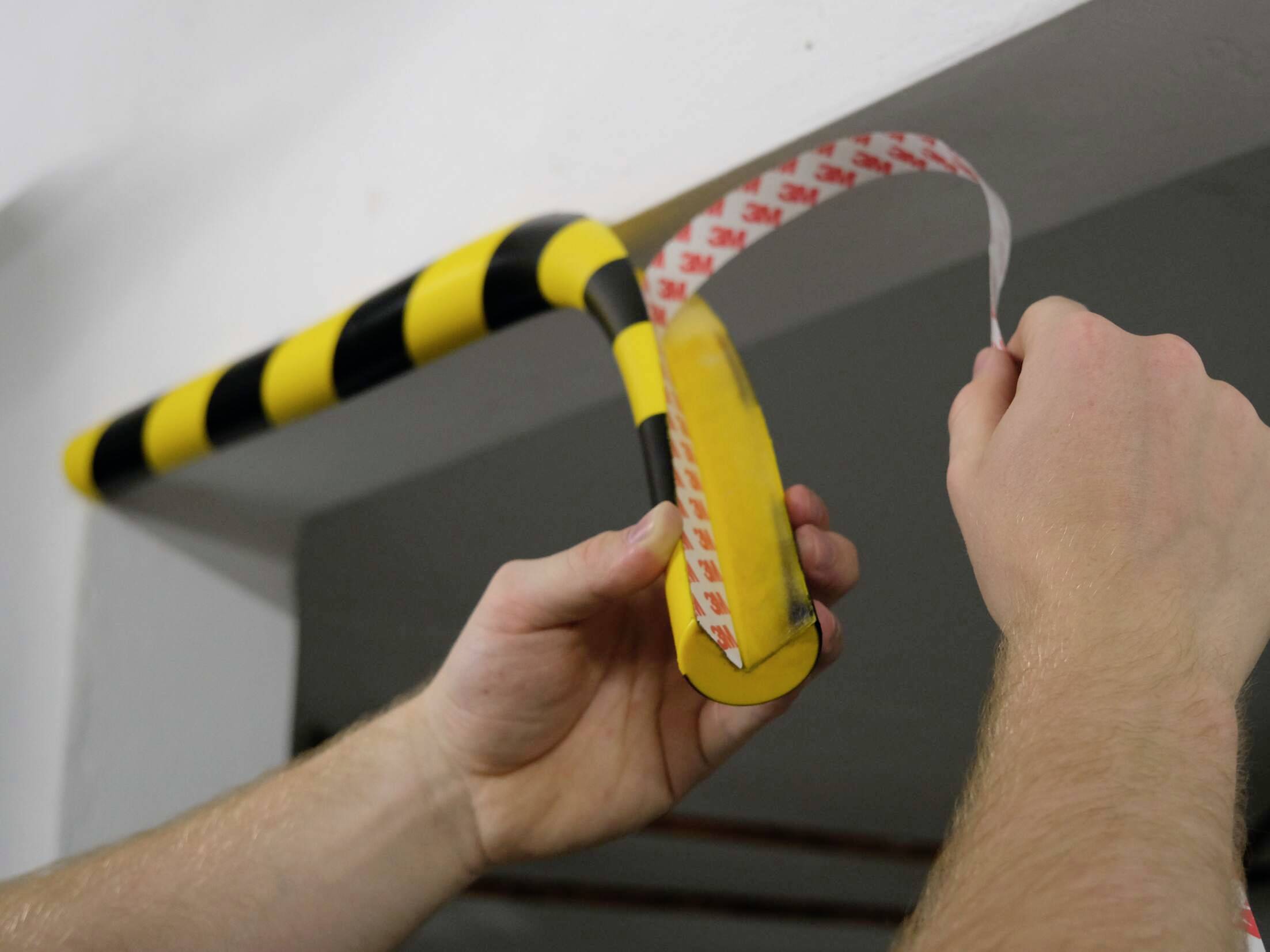 Osoba nakłada czarno-żółtą czapkę ochronną z taśmą dwustronną na krawędzi, podejmując środki bezpieczeństwa.