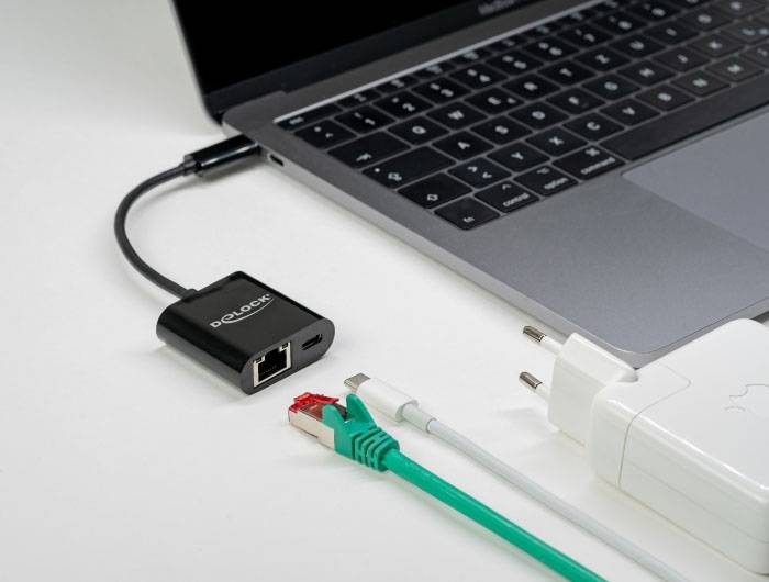 Laptop jest podłączony do czarnej karty sieciowej Ethernet. Obok leży zielony kabel sieciowy, kabel USB i biały zasilacz.