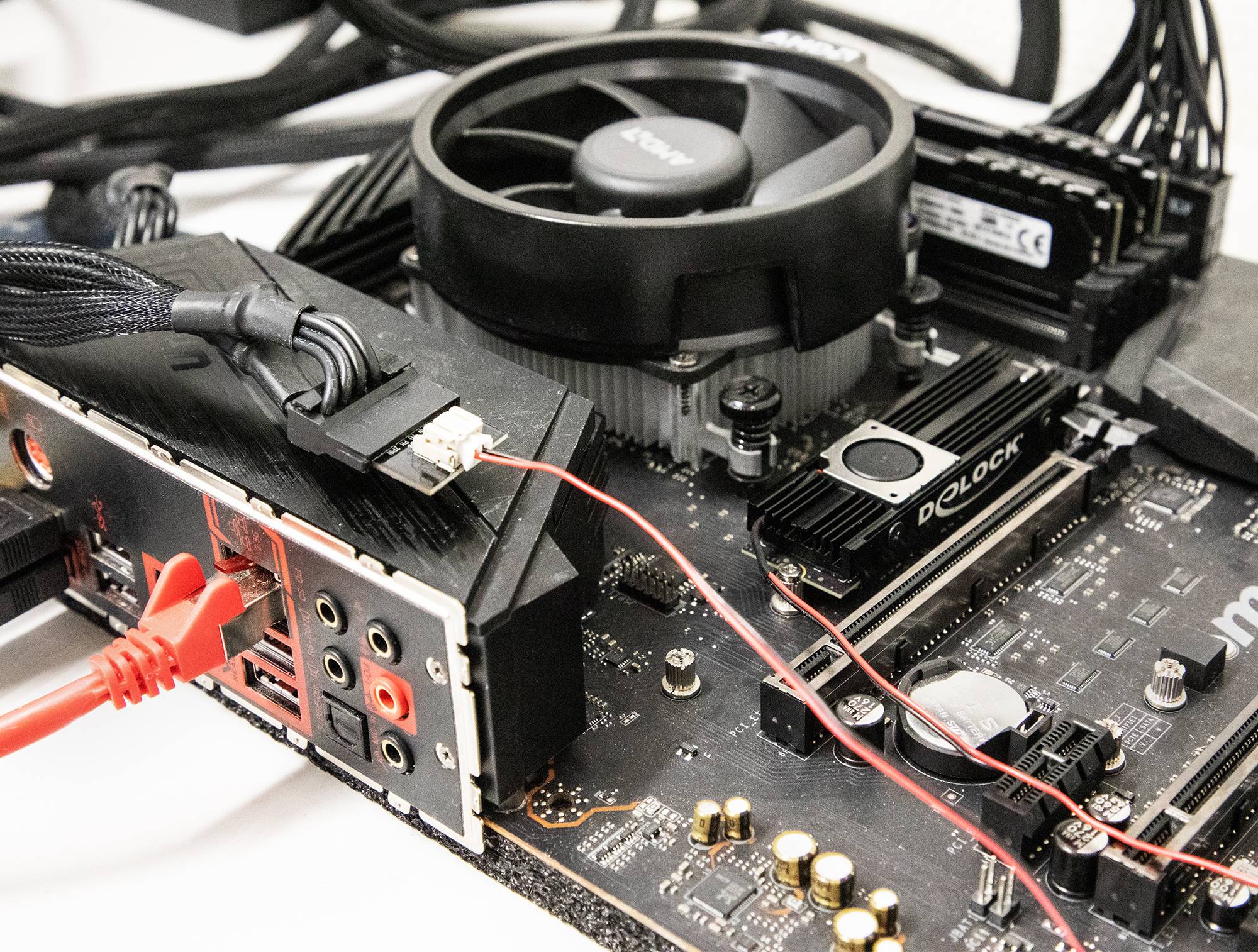 Zbliżenie płyty głównej komputera z zainstalowanym procesorem, chłodzeniem, pamięcią RAM i podłączonymi kablami.