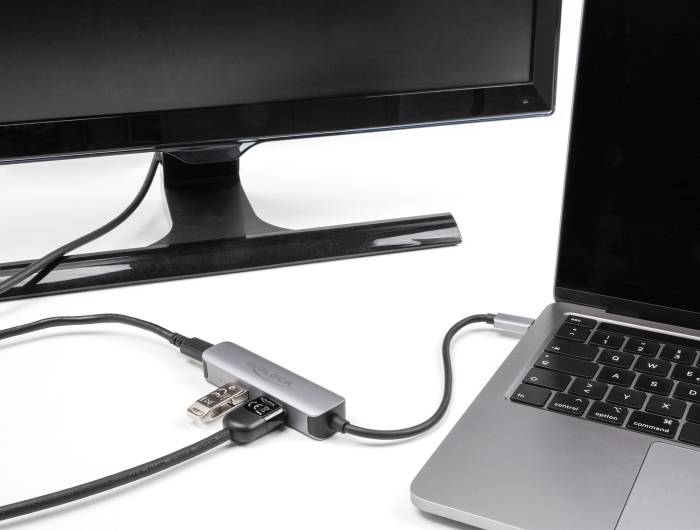 Laptop podłączony do monitora przez hub USB-C. Hub posiada kilka portów i łączy kable między laptopem a ekranem.