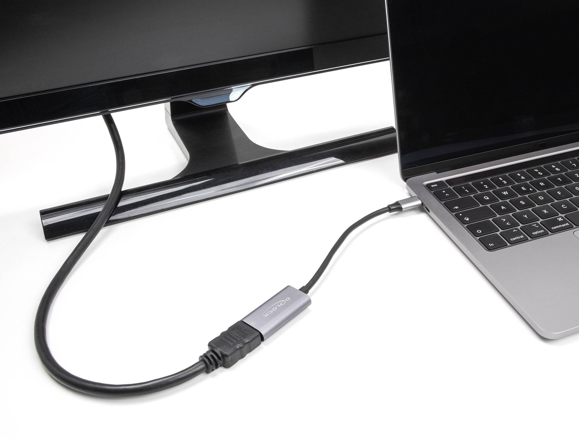 Kabel HDMI łączy laptopa z monitorem. Laptop znajduje się po prawej stronie, monitor po lewej stronie.