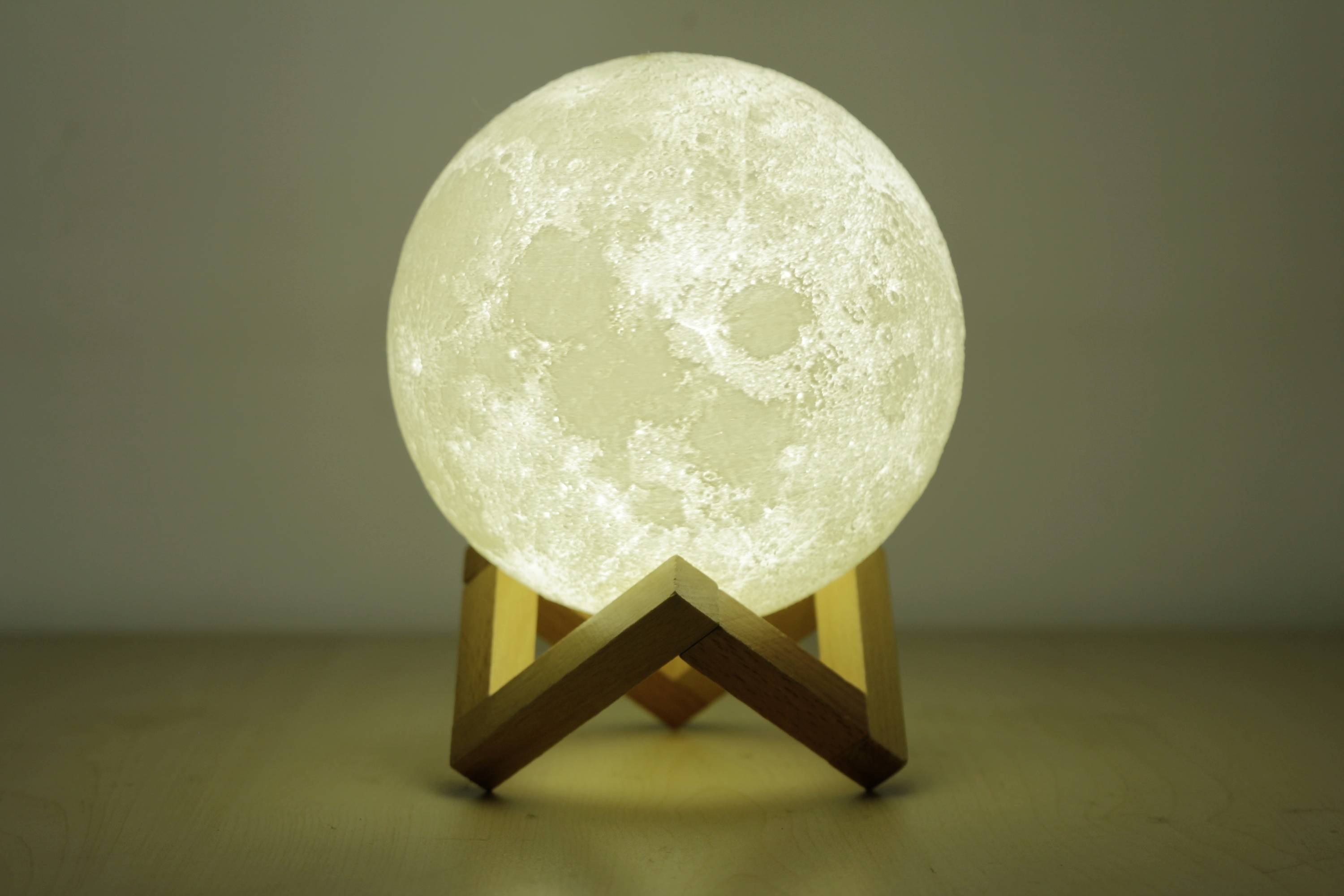 Świecąca lampa w kształcie księżyca na drewnianym stojaku, ukazująca szczegółową powierzchnię księżyca. Ciepłe, kojące światło w ciemnym pomieszczeniu.