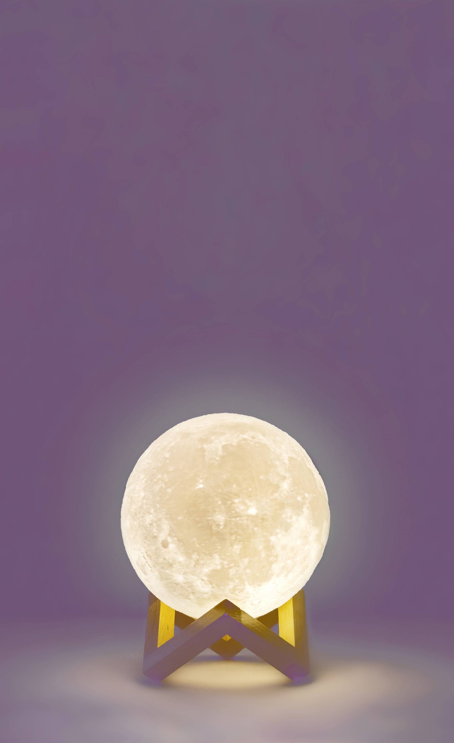 Lampa w kształcie świecącego pełnego księżyca umieszczona na małym drewnianym stojaku na fioletowym tle.