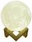 Świecąca lampa księżycowa na drewnianym stojaku, która wygląda jak pełnia księżyca. Emituje miękkie, ciepłe światło.