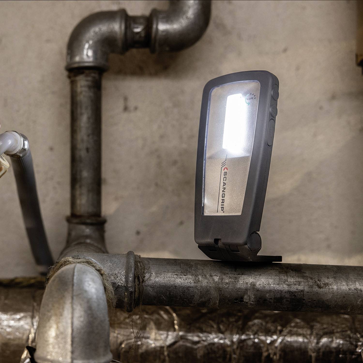 Mała przenośna lampa oświetla szarą rurę w piwnicy lub pomieszczeniu warsztatowym.