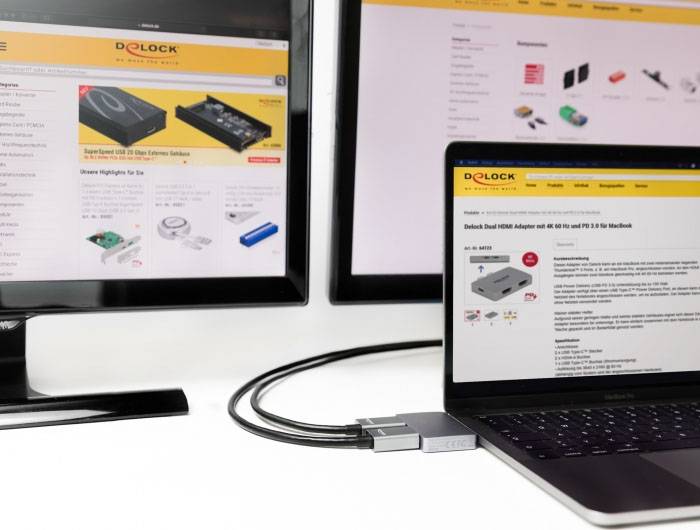 Dwa monitory i laptop wyświetlają stronę produktową z artykułami elektronicznymi. Kable łączą urządzenia między sobą.
