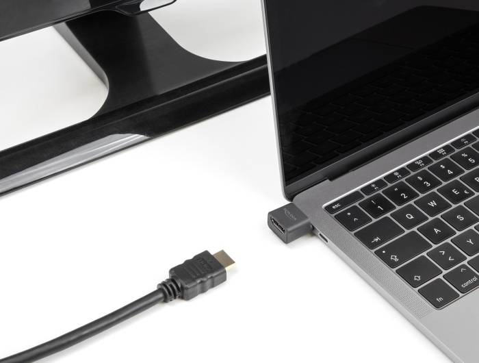 Kabel HDMI leży obok laptopa i podstawki pod monitor. Laptop posiada adapter w porcie USB-C obsługujący złącze HDMI.