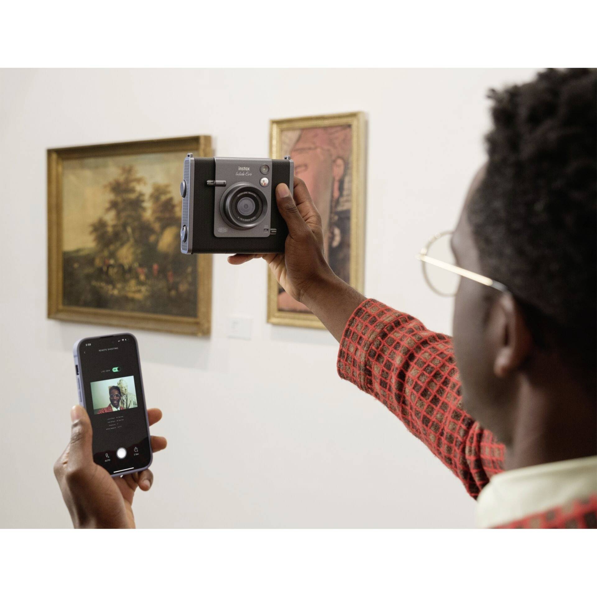 Osoba w muzeum trzyma aparat fotograficzny i smartfon, wygląda na to, że robi zdjęcie obrazu.