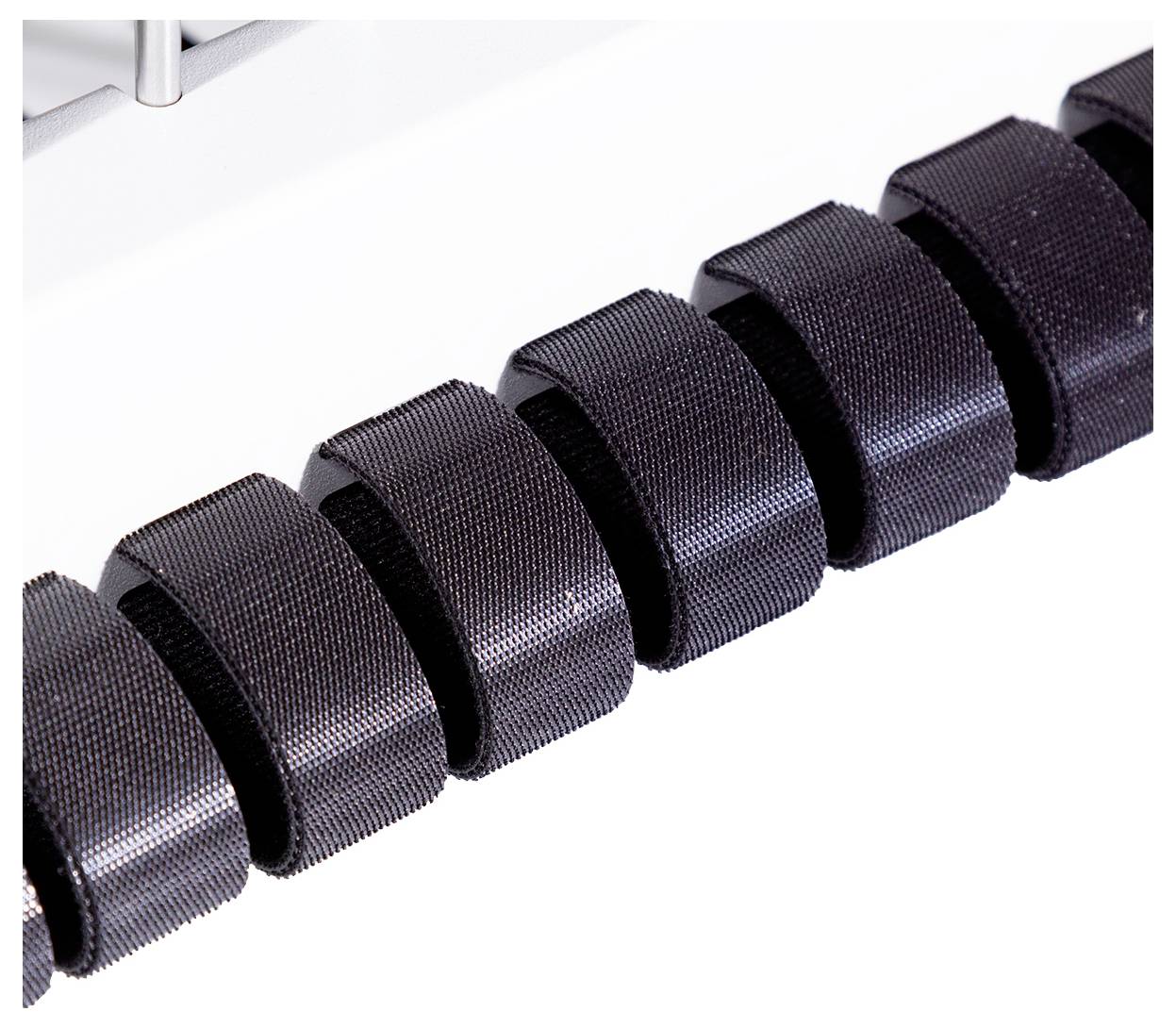 Rząd czarnych, równomiernie rozmieszczonych, prążkowanych rolek w maszynie, prawdopodobnie będących częścią systemu przenośnika.