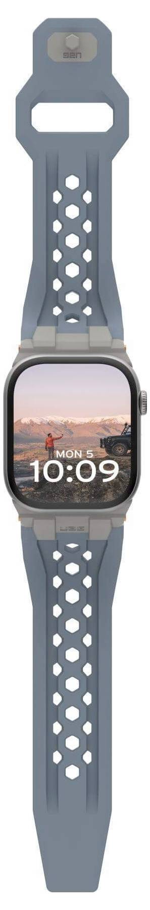 Szara smartwatch z cyfrowym wyświetlaczem czasu '10:09' i tłem przedstawiającym krajobraz miasta o zachodzie słońca.