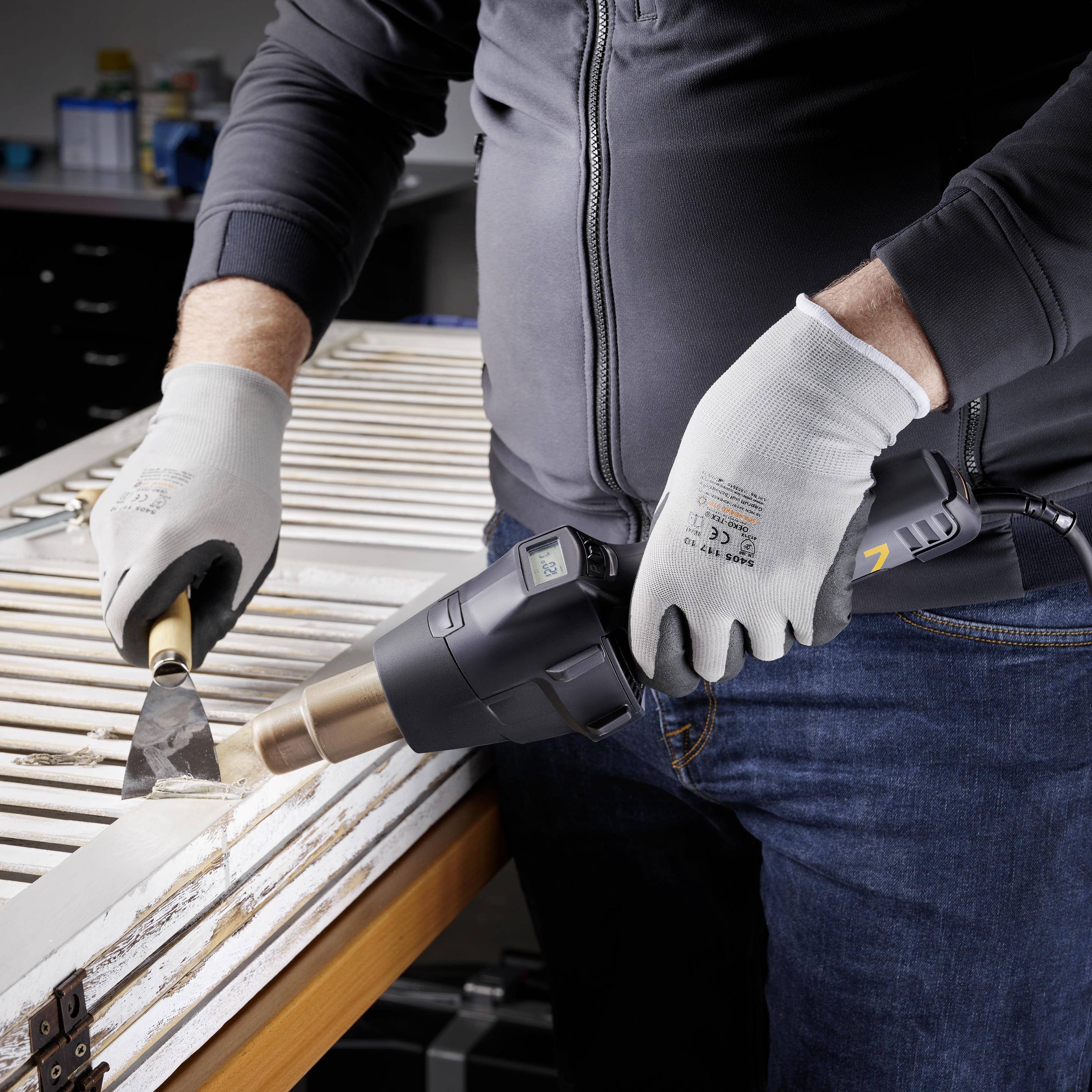 Rzemieślnik usuwa starą farbę z ramy okiennej za pomocą pistoletu na gorące powietrze i skrobaczki.