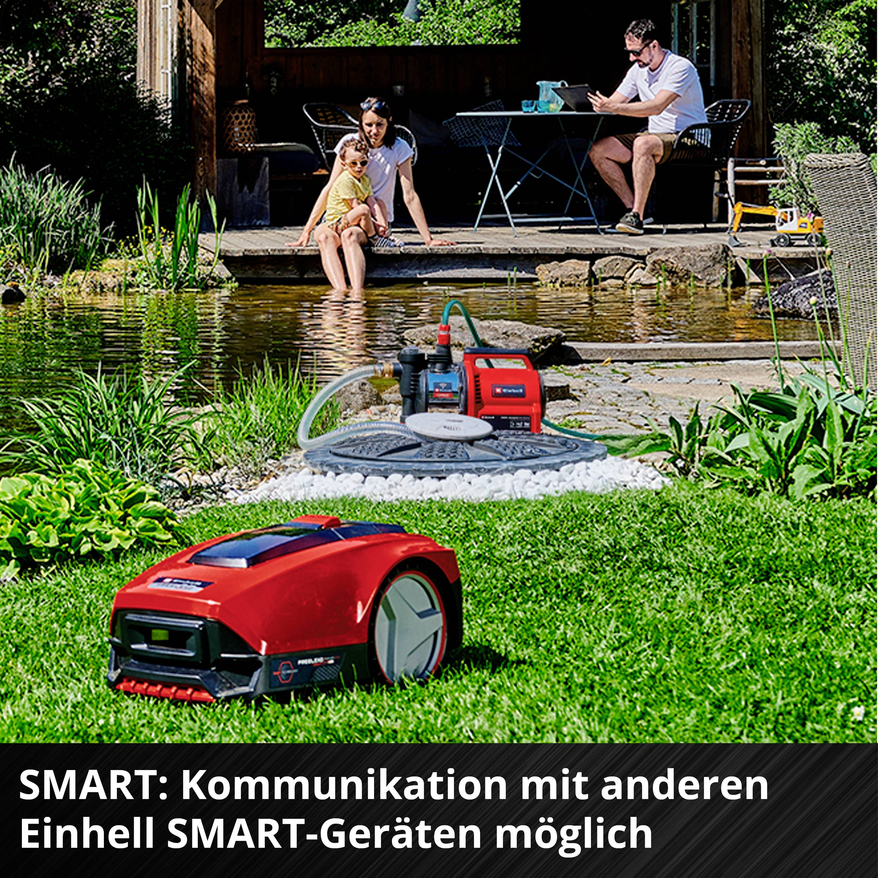 Rodzina siedzi nad stawem. Na pierwszym planie czerwony robot koszący firmy Einhell. Tekst: 'SMART: Możliwość komunikacji z innymi urządzeniami Einhell SMART'.