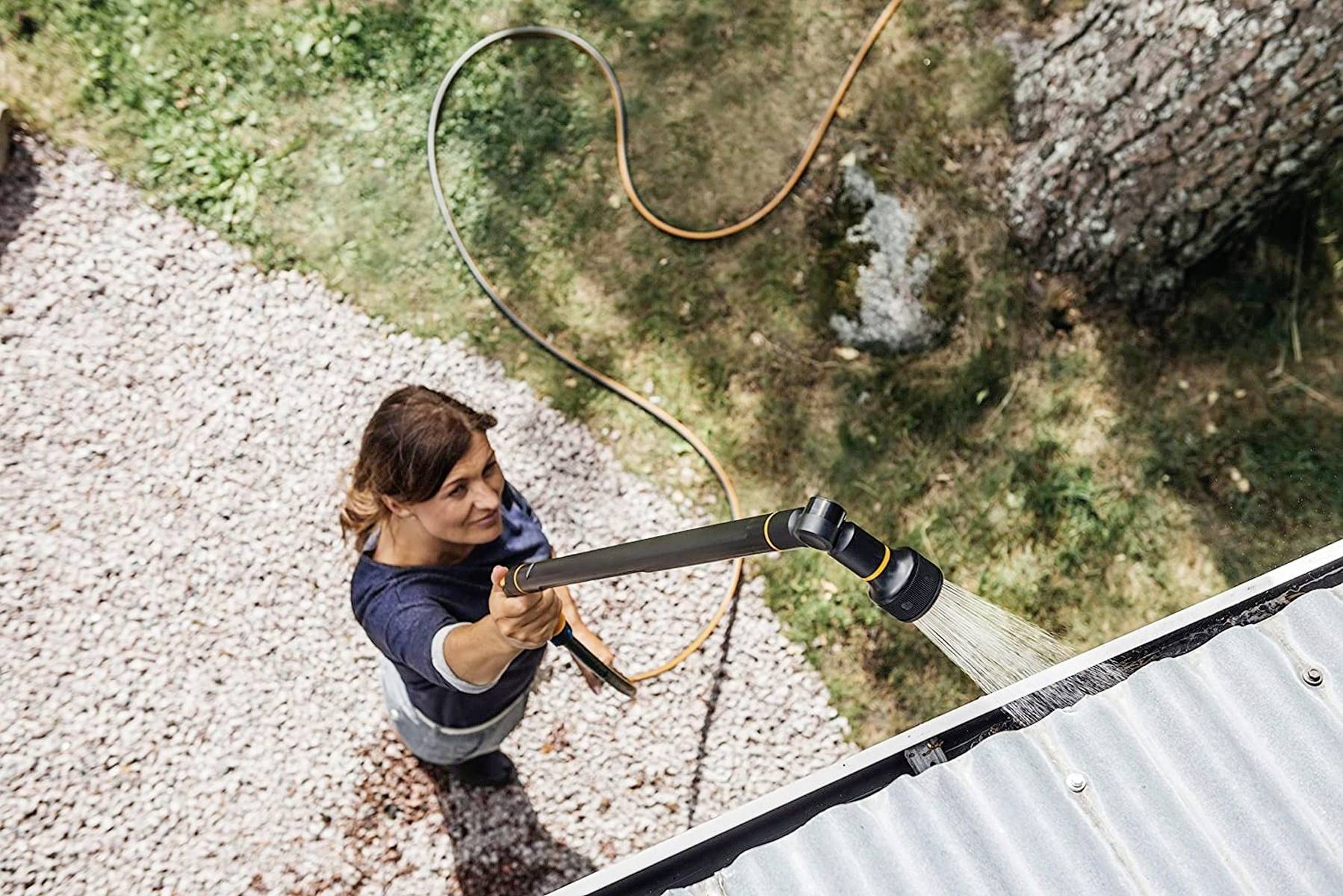 Osoba czyści rynnę za pomocą węża wodnego. Zdjęcie przedstawia czynność z perspektywy z góry.