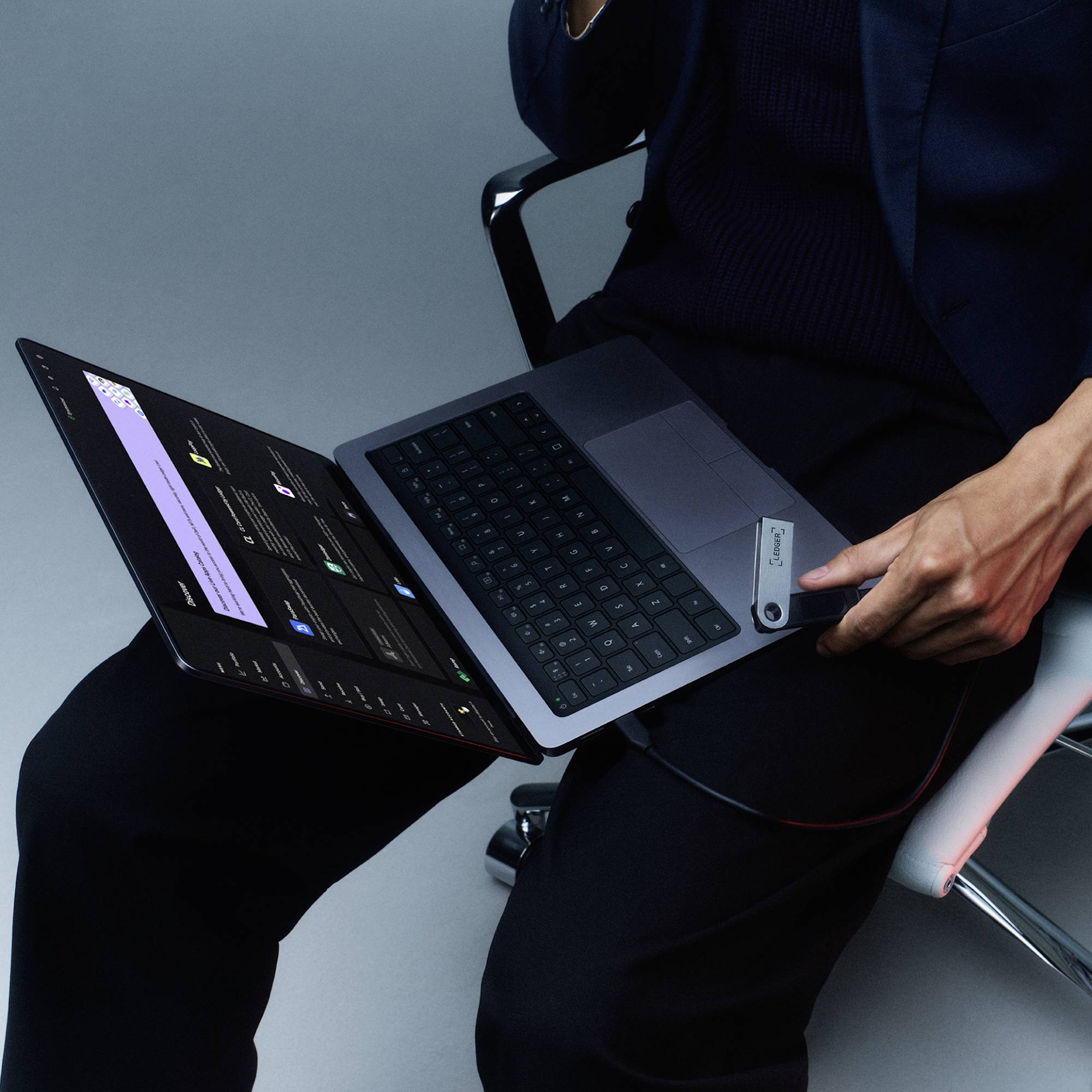 Osoba siedzi na krześle i korzysta z laptopa z dwoma monitorami, jeden z których wyświetla interfejs graficzny.