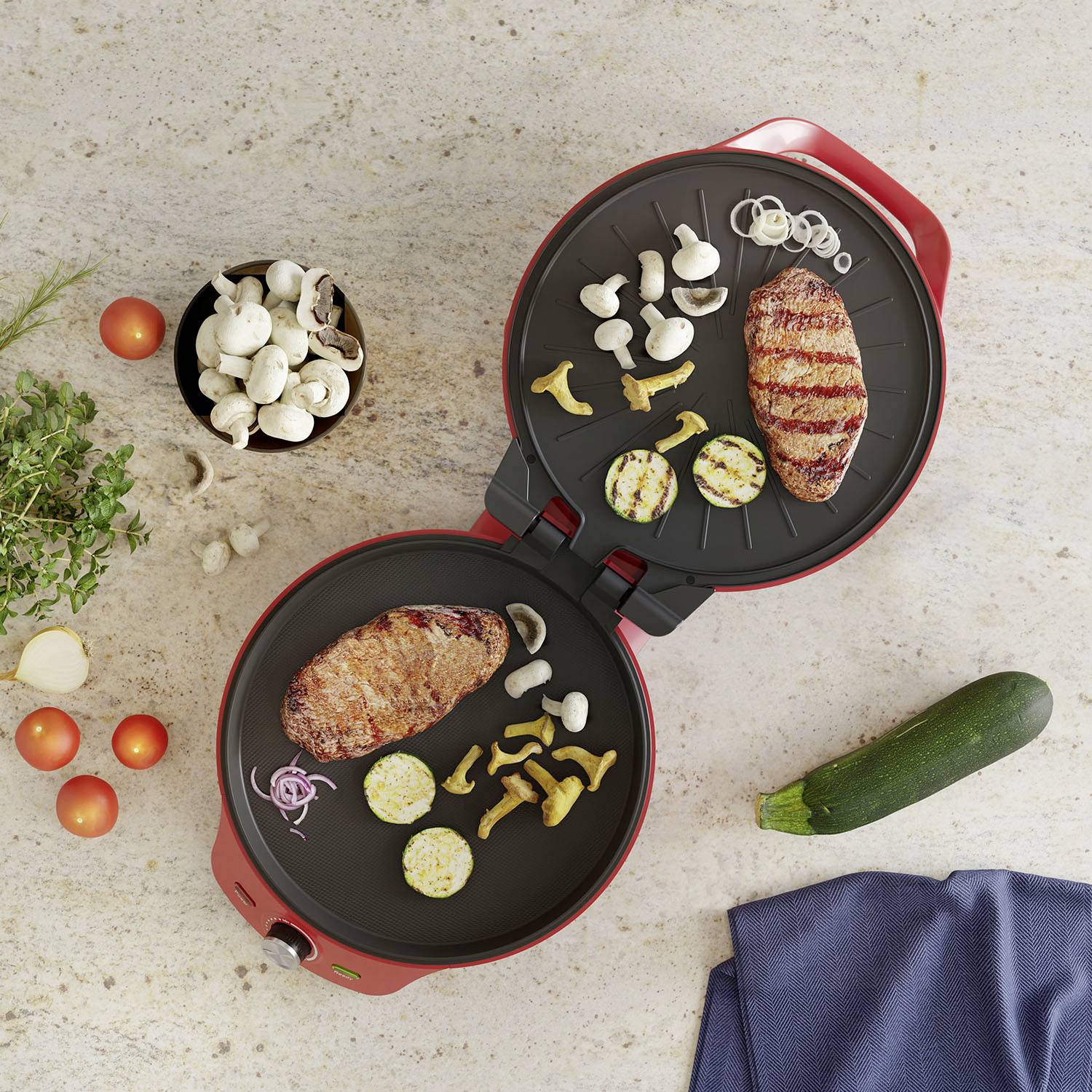 Dwa otwarte elektryczne grille z grillowanym mięsem i warzywami. Obok na stole leżą świeże składniki, takie jak grzyby, pomidory i cukinia.