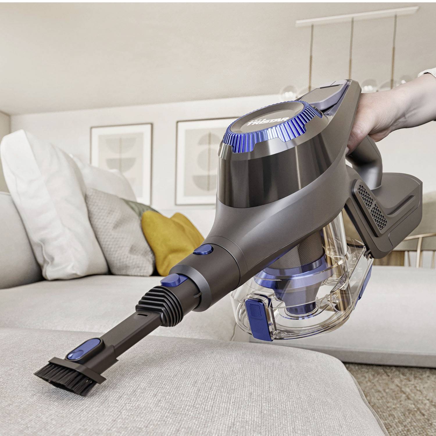 Osoba używa bezprzewodowego odkurzacza ręcznego, aby usunąć kurz z jasnej kanapy. W tle widoczne są poduszki.