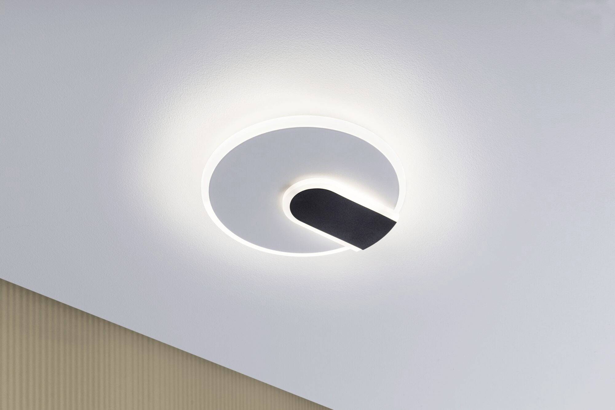 Lampa sufitowa o nowoczesnym, okrągłym designie, z białym pierścieniem LED i czarnym elementem centralnym, na jasnym suficie pomieszczenia.