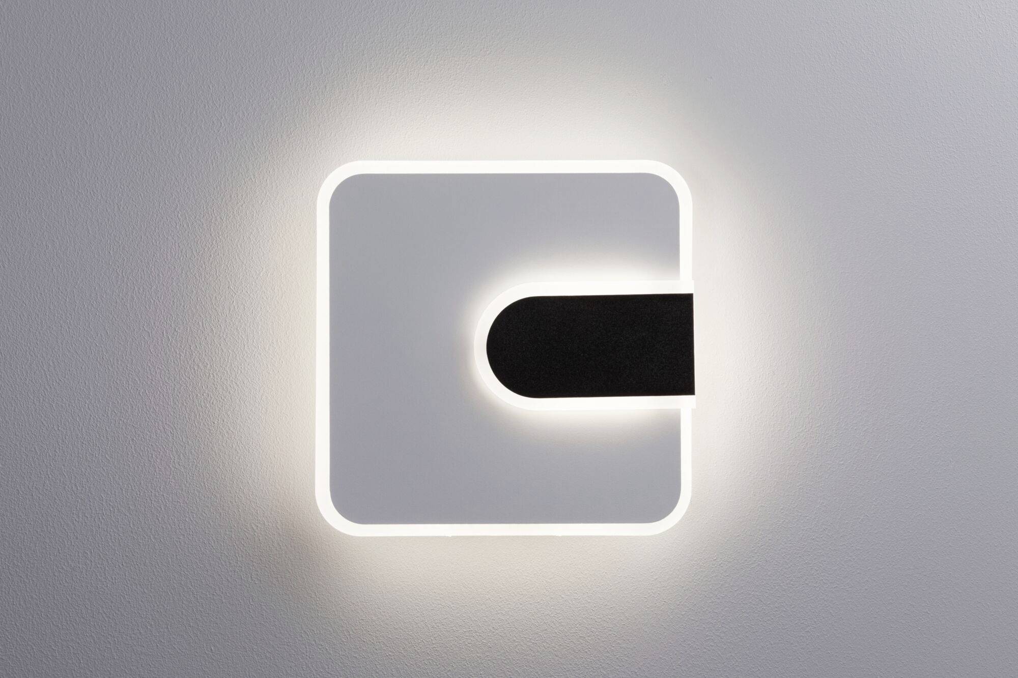 Kwadratowa lampa ścienna z zaokrąglonymi narożnikami i czarnym pasem po prawej stronie, świecąca białym światłem.