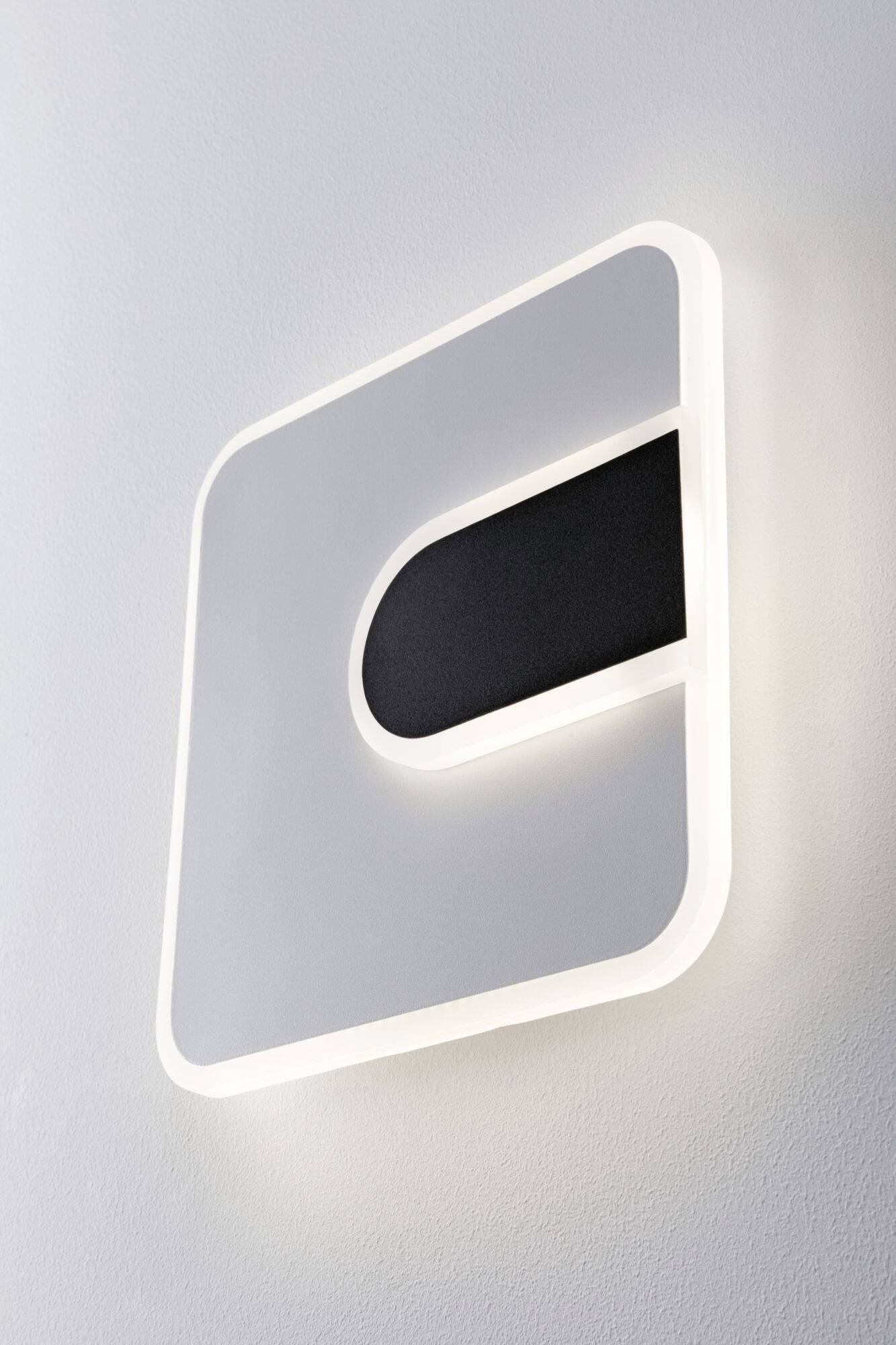 Biała, kwadratowa lampa ścienna z zaokrąglonymi narożnikami i czarnym, prostokątnym elementem wewnątrz, świecąca na ścianie.