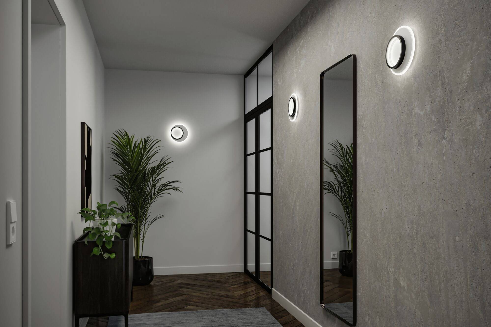 Korytarz z nowoczesnym wystrojem: duża ściana lustrzana, dwie okrągłe lampy ścienne, rośliny doniczkowe, ciemna podłoga w jodełkę.