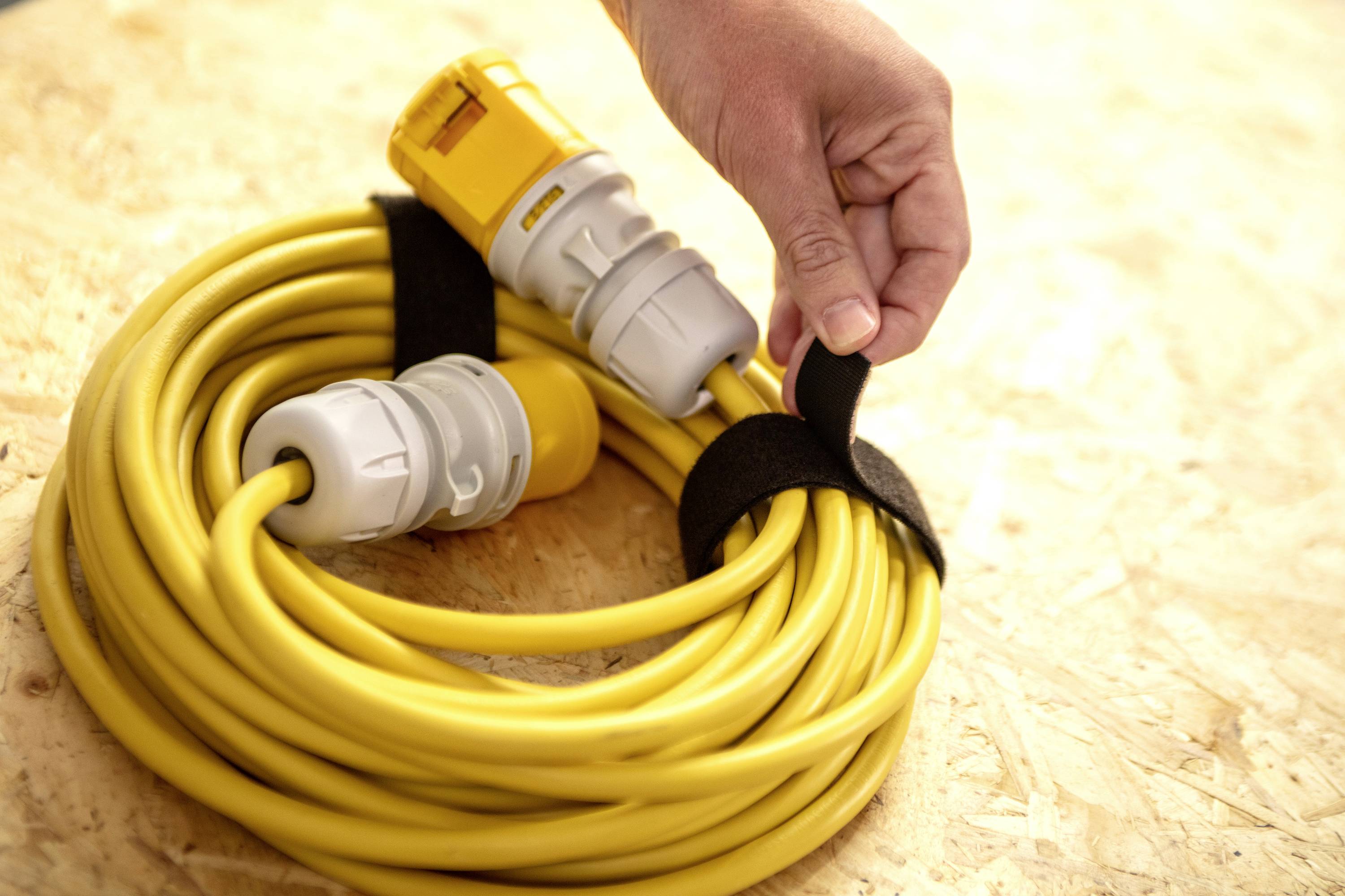 Ręka mocuje żółty kabel przedłużający za pomocą rzepów, leżący na drewnianej powierzchni.