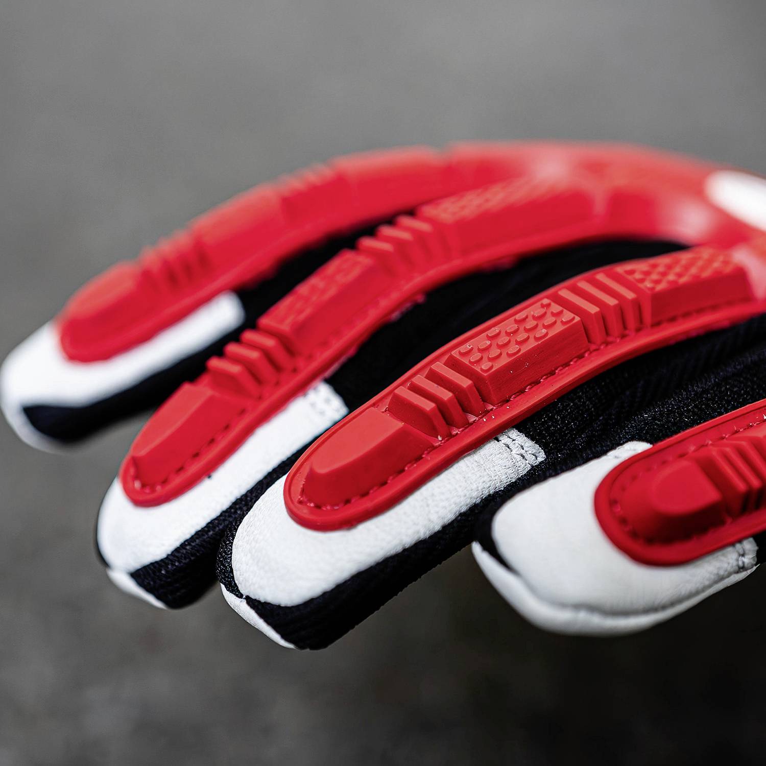 Rękawica motocyklowa do wyścigów w zbliżeniu. Rękawica ma czarno-czerwone i białe elementy, które zapewniają ochronę i przyczepność.