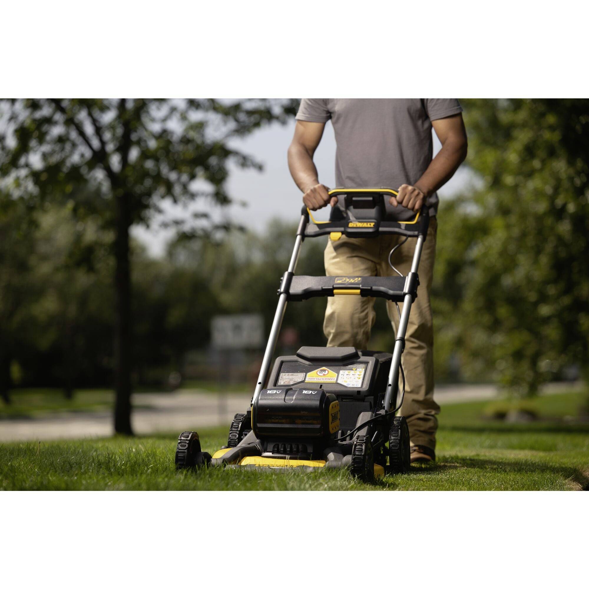 Osoba kosi zieloną trawę kosiarką w świetle dziennym. W tle widać rozmyte drzewa.